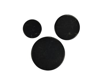 May include: Three black round coasters made of natural stone. The coasters are different sizes.