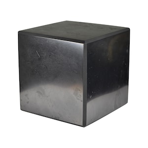 May include: A black cube-shaped pedestal made of a smooth, polished stone. The surface has a subtle sheen and a few faint markings.