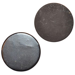 May include: Two dark gray, circular objects are displayed against a white background. The objects have a slightly textured surface with subtle variations in color. The overall appearance suggests a vintage or antique aesthetic.