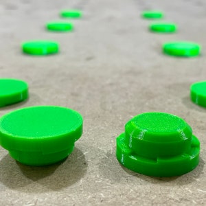 May include: Bright green, 3D-printed, circular objects. The objects are arranged in a line, with some in focus and others blurred in the background. The objects have a layered design, with a flat top and a slightly wider base.