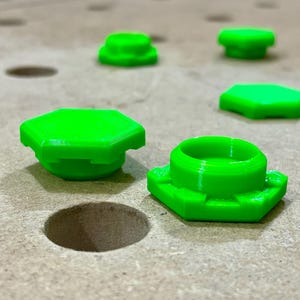 May include: Five bright green plastic hexagonal caps, some with a raised center, on a light brown surface.