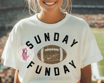 Può includere: T-shirt bianca con le parole "SUNDAY FUNDAY" in nero sopra e sotto una grafica di football americano marrone. La maglietta presenta anche un piccolo logo circolare con testo e un'immagine a cartoni animati.