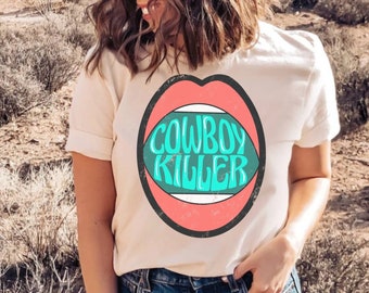 May include: White t-shirt with a graphic of a red mouth with a green and turquoise oval inside that says "COWBOY KILLER".