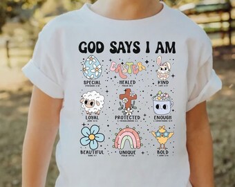 May include: White t-shirt with the text "God Says I Am Easter" and colorful illustrations of Easter-themed items, each with a Bible verse. The illustrations include an egg, a bunny, a lamb, a cross, a cup, a flower, a rainbow, and a chick.