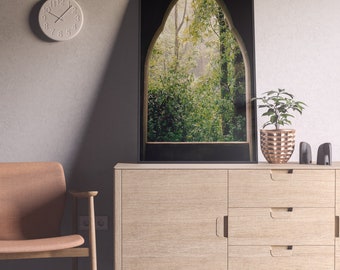 May include: A light wood cabinet with three drawers and a door. The cabinet is in a room with a clock on the wall and a framed picture of a forest scene above the cabinet.