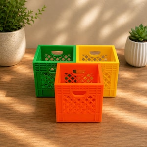 May include: Three small, square storage crates in bright orange, yellow, and green. Each crate features a lattice-style grid pattern on the sides, a solid base, and a cutout handle on the top edge of each side for easy carrying and organization.