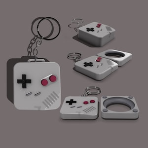May include: A white and gray keychain shaped like a retro video game controller with red buttons. The keychain is attached to a silver ring.