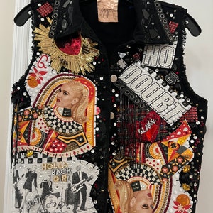May include: A black denim vest featuring a variety of patches and embellishments, including a red heart with gold sequins, a playing card with a woman's face, a band photo with the text "Hollah Back Girl", and a white patch with the text "No Doubt".