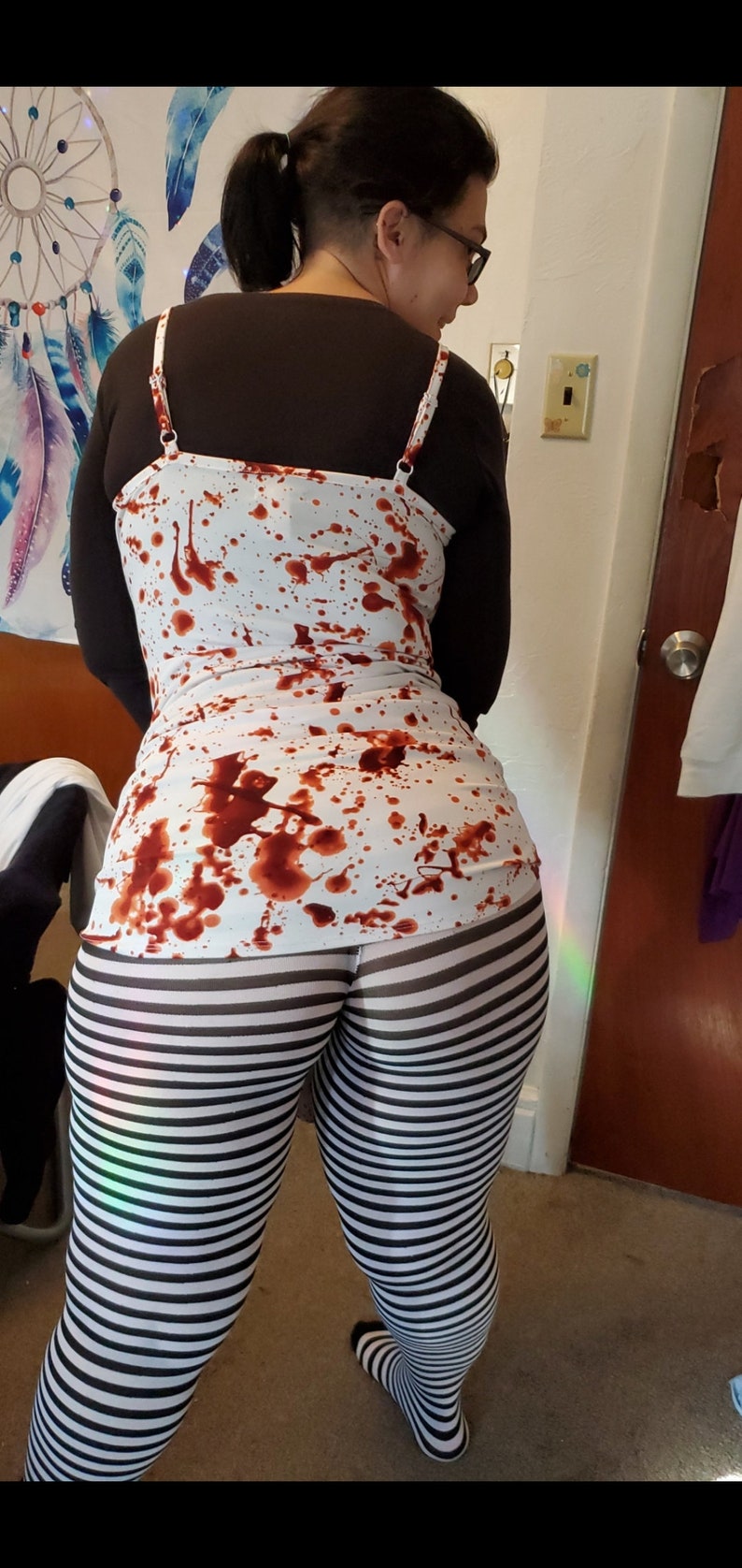 May include: A white tank top with red splatter paint design, worn over black leggings with white stripes.