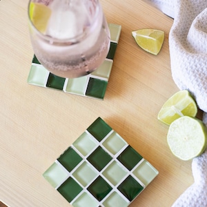 Könnte beinhalten: Zwei Untersetzer aus grünen und weißen Mosaikfliesen mit einem Glas rosa Limonade auf einem der Untersetzer. Auf einem weißen Handtuch liegen außerdem Limettenspalten.