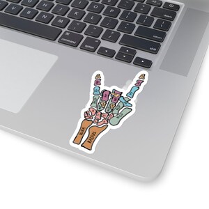 Puede incluir: Una pegatina de una mano haciendo el gesto de rock and roll. La mano es un esqueleto con los huesos etiquetados en diferentes colores. Los huesos est&aacute;n etiquetados con los nombres de los huesos, como ulna, radio, MCP y PIP.