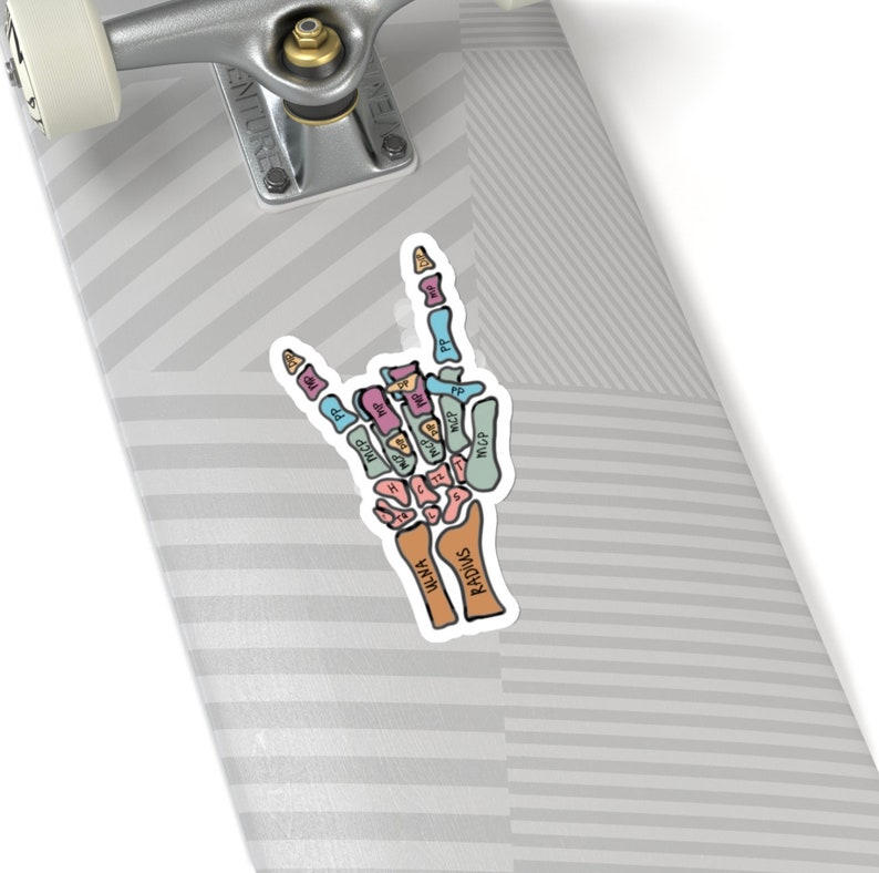 Puede incluir: Una pegatina de una mano de esqueleto haciendo el gesto de rock and roll. Los huesos est&aacute;n etiquetados con sus nombres anat&oacute;micos en diferentes colores. El texto "RADIUs" y "ULNA" est&aacute; escrito en los huesos del antebrazo.