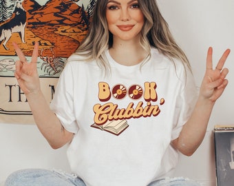 May include: White t-shirt with a retro-style graphic that says "Book Clubbin'" with a book and record player design.