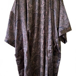 May include: A long, open-front robe featuring a dark brown and black paisley pattern with subtle pink accents. The garment has wide, three-quarter length sleeves, a straight hemline, and two large patch pockets positioned on the lower front panels.