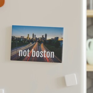 May include: A photograph of a city skyline with a highway in the foreground. The text "not boston" is printed below the image.