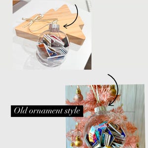 May include: Two clear glass Christmas ornaments filled with miniature books. The ornament on the left is on a wooden surface, while the ornament on the right is hanging on a pink artificial Christmas tree. The text "New ornament style as of December 1st, 2024" is above the left ornament, and the text "Old ornament style" is below the right ornament.