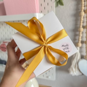 May include: A white gift box with a yellow satin ribbon tied in a bow. The box has a pink circle sticker with the text "made with love" on it.