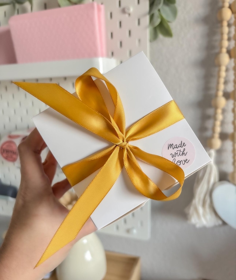 May include: A white gift box with a yellow satin ribbon tied in a bow. The box has a pink circle sticker with the text "made with love" on it.
