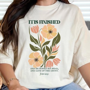 May include: A white t-shirt with a floral design and the text "IT IS FINISHED" and "AND HE BOWED HIS HEAD, AND GAVE UP THE GHOST. JOHN 19:30".