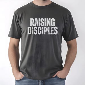 May include: A dark gray t-shirt with the text "RAISING DISCIPLES" printed in white on the front.