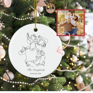 May include: A white ceramic Christmas ornament with a family line drawing and a photo. The ornament features a line drawing of a family of three, with the text "The Crawfords" and "Christmas 2024". The photo shows the family.