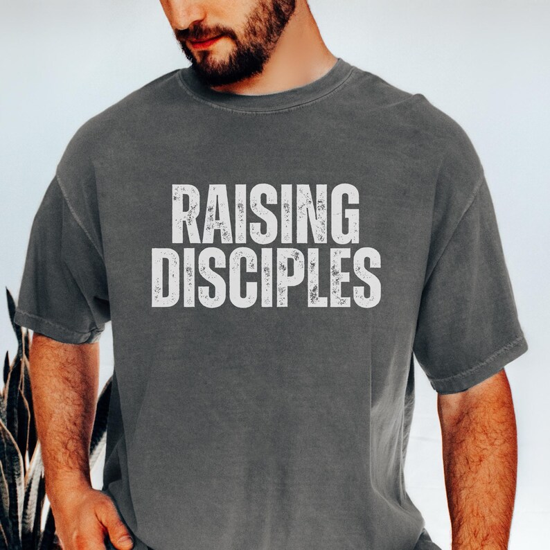 May include: A dark gray t-shirt with the text "RAISING DISCIPLES" printed in white on the front.