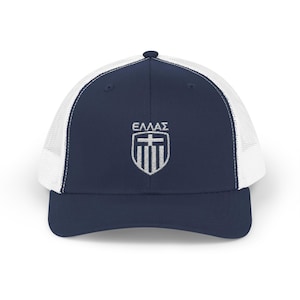 May include: Navy blue and white trucker cap. The front panel is navy blue with the Greek word "ΕΛΛΑΣ" above a white emblem. The emblem features a cross and vertical stripes. The back of the cap is white mesh.