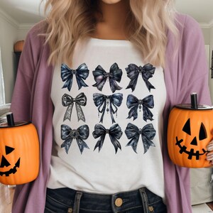 May include: A white t-shirt with a design of twelve black and silver bows. The bows are arranged in four rows of three. The bows have different designs, including lace, jewels, and ribbons.
