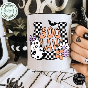 May include: White ceramic mug with a black rim and handle, featuring a Halloween-themed design. The design includes the words "BOO HAW" in orange, a ghost, flowers, and a bat. The mug also has a horseshoe and a checkered pattern.