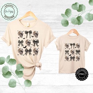 May include: Two beige t-shirts, one adult and one child size, displayed on wooden hangers. Each shirt features a repeating pattern of floral skull designs, black bows, bats, and stars. The shirts are labeled "Original Designer" and "Digital Download".