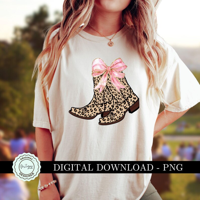 K&ouml;nnte beinhalten: Ein wei&szlig;es T-Shirt mit einem Design aus zwei Cowboy-Stiefeln im Leopardenmuster mit einer rosafarbenen Schleife oben. Der Text "DIGITAL DOWNLOAD - PNG" befindet sich am unteren Rand des Shirts.