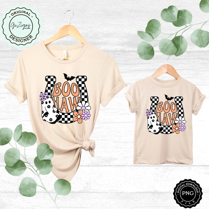May include: Two beige t-shirts, one adult and one child size, with a Halloween-themed design. The design features a horseshoe with the words "BOO HAW", a ghost, flowers, and a bat. The horseshoe has a black and white checkered pattern.