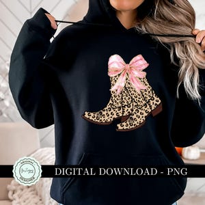 K&ouml;nnte beinhalten: Ein schwarzer Hoodie mit einem Grafikdruck von Cowboystiefeln mit Leopardenmuster und einer rosafarbenen Schleife. Der Text "DIGITALER DOWNLOAD - PNG" ist unter dem Grafikdruck aufgedruckt.
