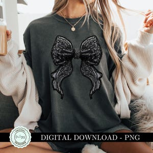May include: A dark gray sweatshirt with a large black rhinestone bow design. The bow is made of a mesh fabric with rhinestones.