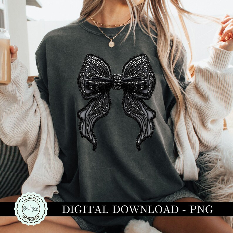 May include: A dark gray sweatshirt with a large black rhinestone bow design. The bow is made of a mesh fabric with rhinestones.