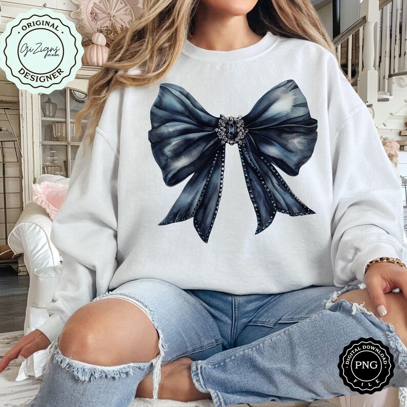 May include: A white sweatshirt with a large blue bow with rhinestones on it. The bow is centered on the sweatshirt and is the main focus of the image. The sweatshirt is being worn by a person, but the person's face is not visible.