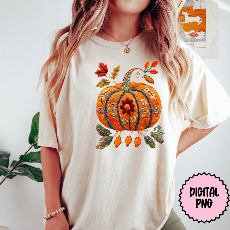 Peut inclure: Un t-shirt blanc avec un motif de citrouille brod&eacute;. La citrouille est orange avec des feuilles et des fleurs vertes. Le motif est de style vintage. "Digital PNG" est &eacute;crit sur un cercle rose dans le coin inf&eacute;rieur droit de l'image.