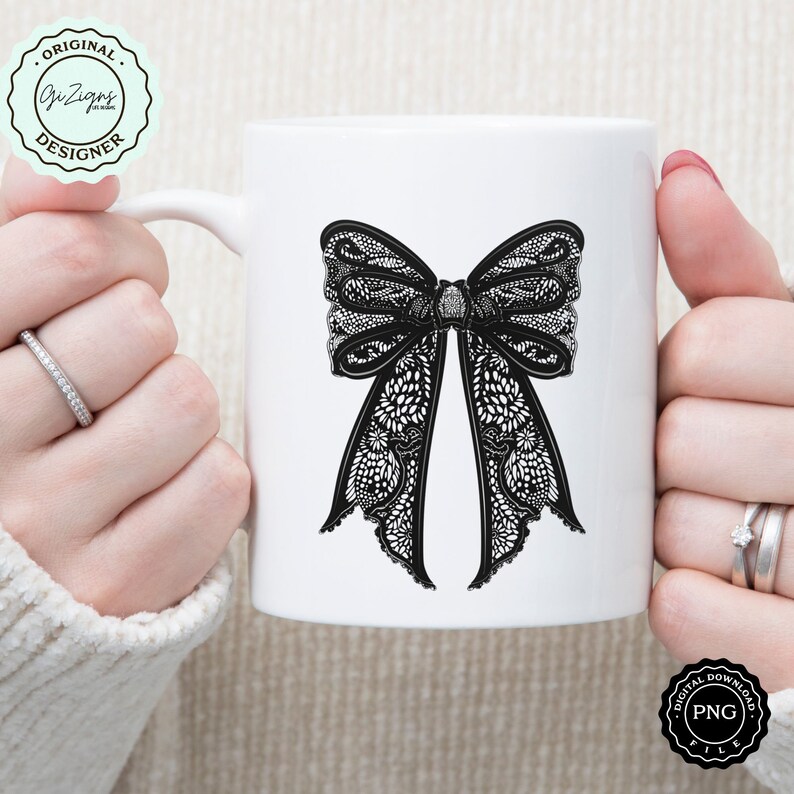 May include: White ceramic mug with a black lace bow design. The mug is held by a hand.