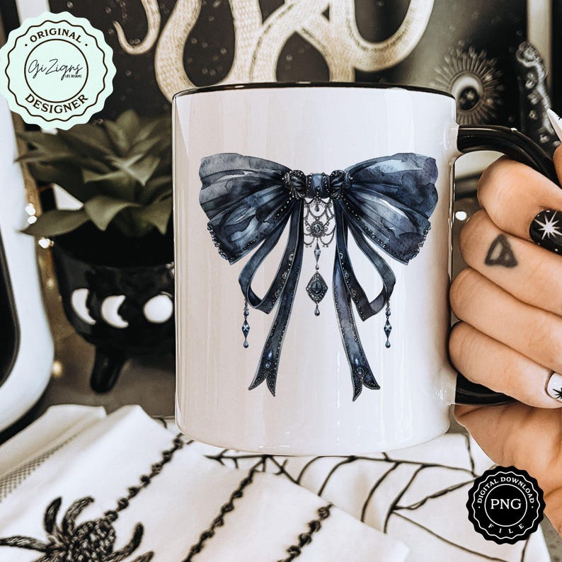 May include: White ceramic mug with a black rim and handle. The mug features a watercolor illustration of a large black bow with a silver and black pendant.