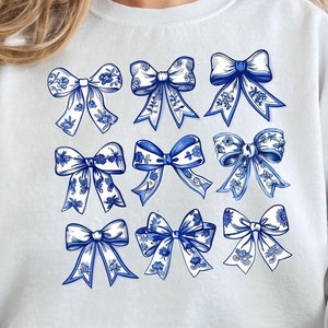 May include: A white sweatshirt with a blue and white pattern of bows. The bows are all different sizes and shapes, and they are arranged in a grid pattern.
