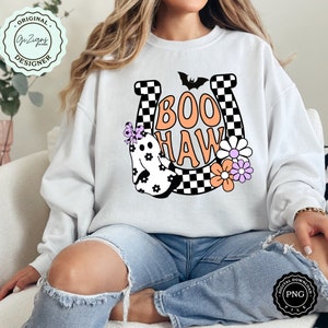 May include: White sweatshirt with a colorful Halloween-themed graphic. The design features a ghost, flowers, a horseshoe, and the words "Boo Haw" in orange. A bat graphic is above the text. The sweatshirt is a digital download.