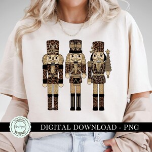 May include: Three nutcracker figurines with gold glitter and leopard print designs. The nutcrackers are wearing hats and have a Christmas tree design.