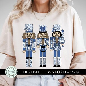 May include: Three blue and white nutcracker figurines with a blue and white floral pattern. The nutcrackers are holding a drum, a candy cane, and a Christmas tree. The text "DIGITAL DOWNLOAD - PNG" is at the bottom of the image.