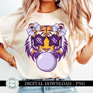 May include: Cream-colored t-shirt featuring a tiger face design with purple and yellow accents. The tiger wears star-shaped sunglasses and has purple bows on its head. A large bubblegum bubble is in front of the tiger's face. Text reads "DIGITAL DOWNLOAD - PNG".