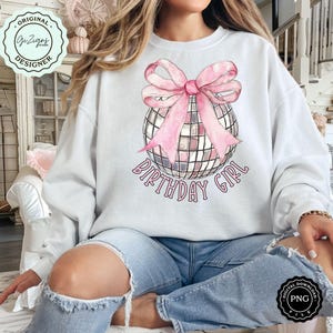Op de afbeelding: Een wit sweatshirt met een roze strik op een zilveren discobal. De tekst "Birthday Girl" is onder de discobal gedrukt.