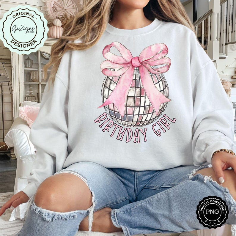 Op de afbeelding: Een wit sweatshirt met een roze strik op een zilveren discobal. De tekst "Birthday Girl" is onder de discobal gedrukt.