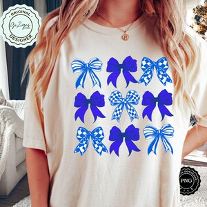 May include: A white t-shirt with a design of nine blue and white bows. The bows are arranged in a grid pattern. The bows are all different designs, some are checkered, some are striped, and some are solid blue.