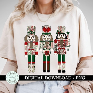 May include: Cream-colored t-shirt featuring three festive nutcracker illustrations. Each nutcracker is adorned with red, green, and floral patterns, and they are standing in a row. The text "DIGITAL DOWNLOAD - PNG" is displayed below the illustrations.