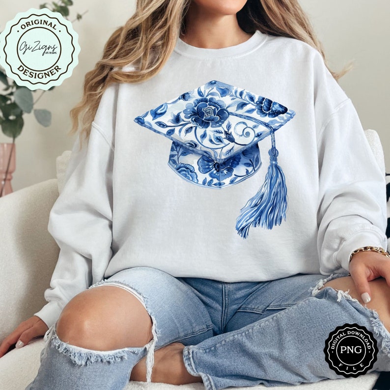May include: A white sweatshirt with a blue and white floral graduation cap design. The cap has a tassel and is a watercolor style illustration.