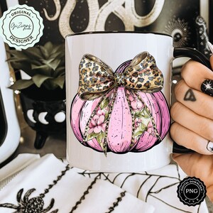 Pode incluir: Caneca de cer&acirc;mica branca com uma ab&oacute;bora rosa com um la&ccedil;o de estampa de leopardo e detalhes florais. A caneca tem uma borda e uma al&ccedil;a pretas.